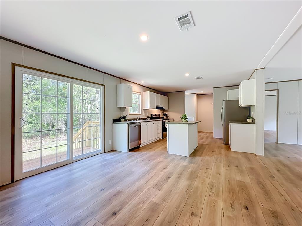 A kitchen with white cabinets, a center island, and wood-look flooring opens to a patio — 115 BETSY ROSS PLACE, SATSUMA, FL