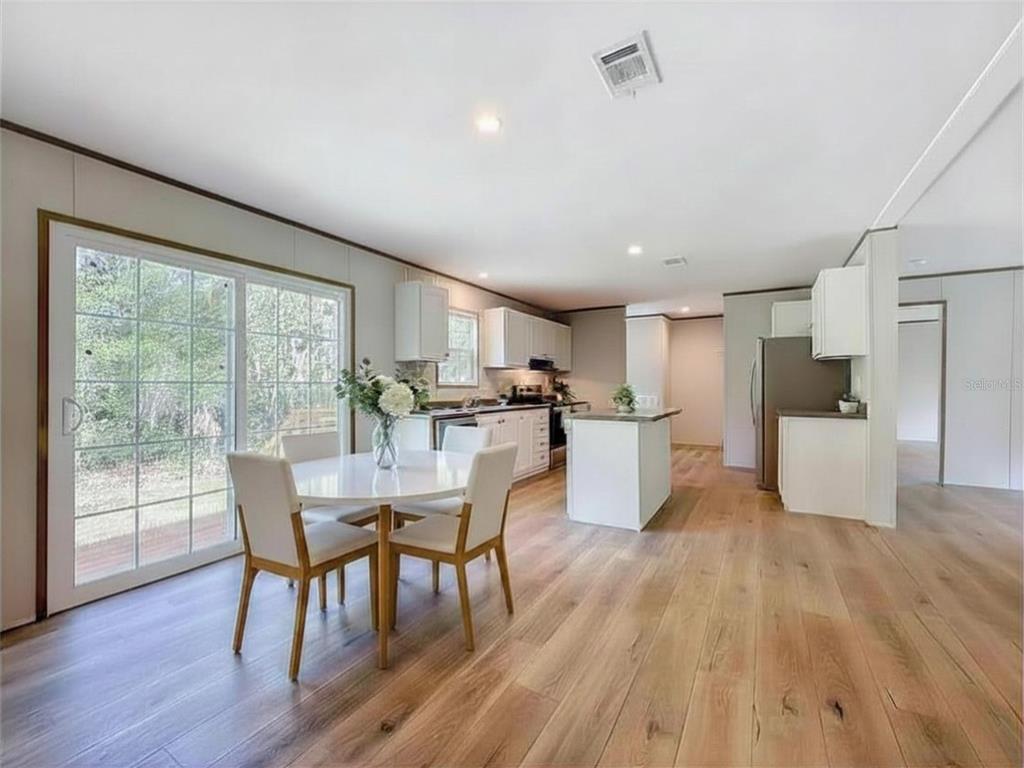 A dining area and kitchen with white cabinets, a center island, and wood-look flooring — 115 BETSY ROSS PLACE, SATSUMA, FL