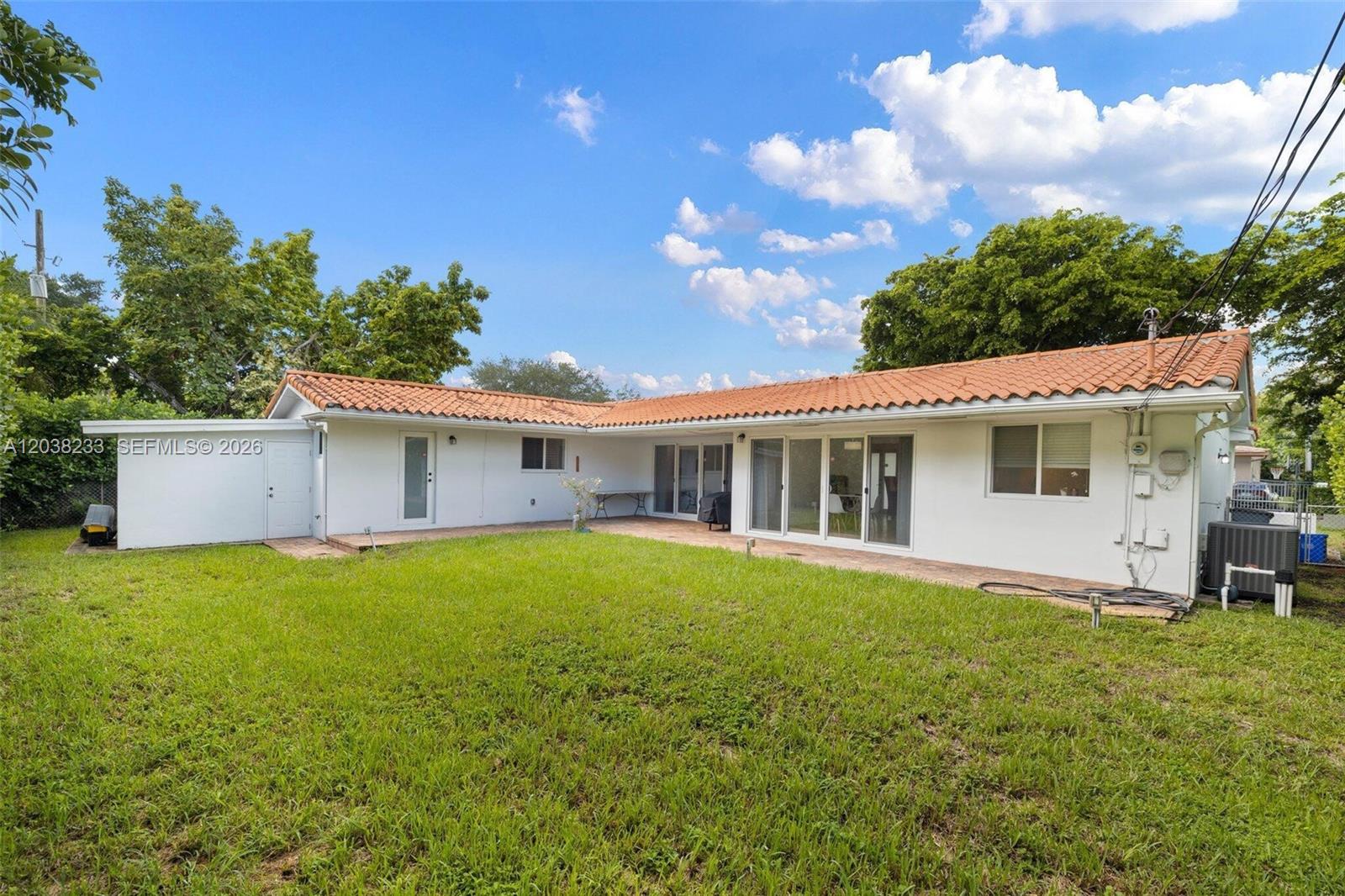 The exterior of a white, single-story house features a red tile roof and a backyard — 811 Capri St, Coral Gables FL 33134, CORAL GABLES, FL