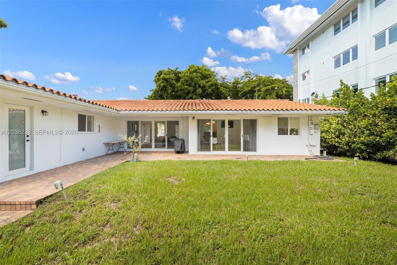 The exterior of a white house features a tiled roof, sliding glass doors, and patio — 811 Capri St, Coral Gables FL 33134, CORAL GABLES, FL