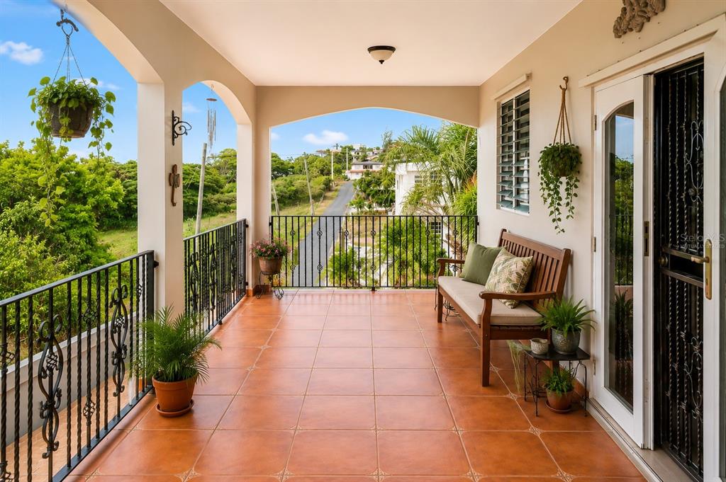 A covered balcony with terracotta tile flooring, a wooden bench, and black metal railings — 8466 CALLE LOS LUGO, QUEBRADILLAS, PR