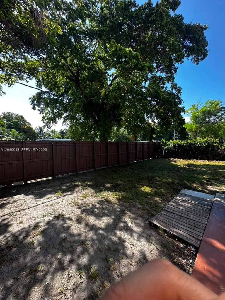 A backyard features a wooden fence, a large tree, and a small wooden platform — 1201 NE 148th St # B, Miami FL 33161, MIAMI, FL