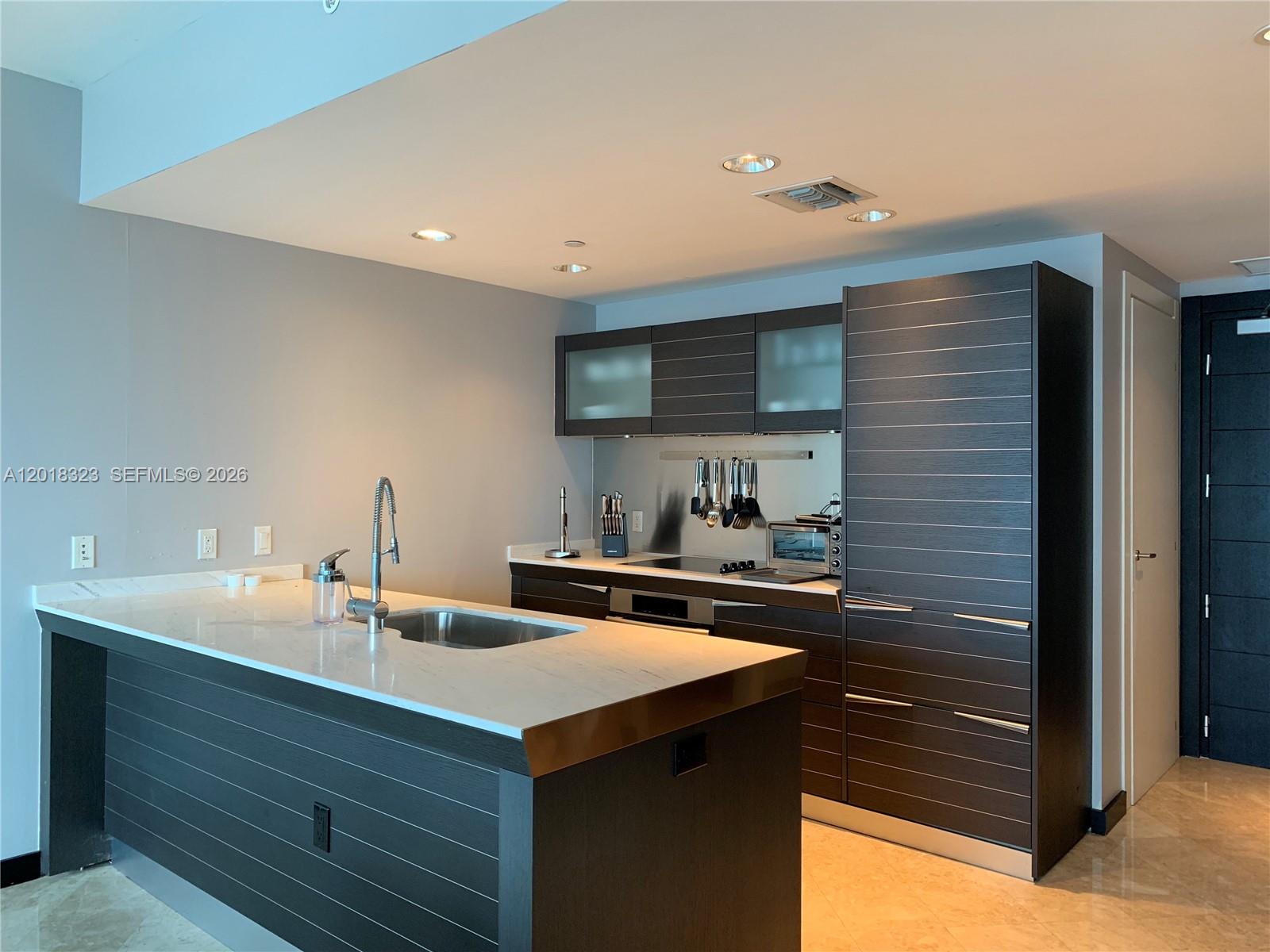 A modern kitchen features dark wood cabinetry, a white marble island, and stainless steel appliances — 200 Biscayne Boulevard Way # 4212, Miami FL 33131, MIAMI, FL