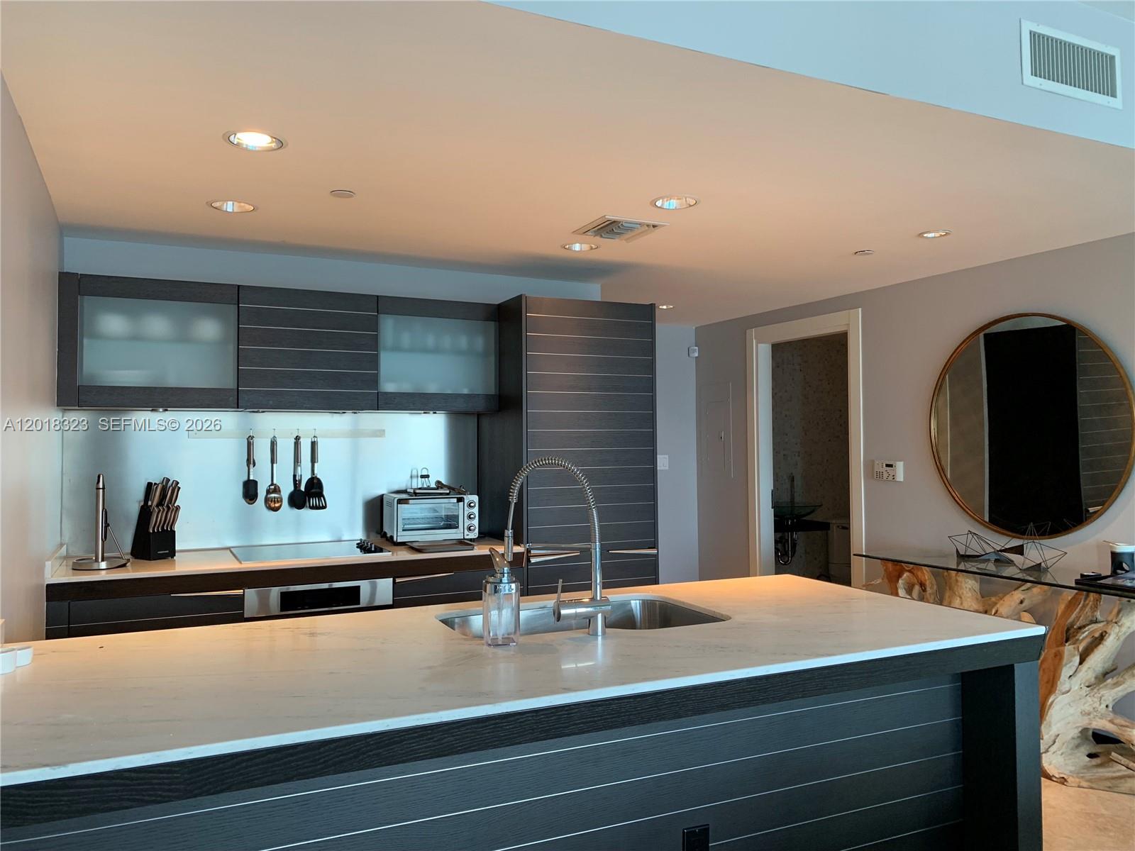 A modern kitchen features dark wood cabinetry, a white marble island, and stainless steel appliances — 200 Biscayne Boulevard Way # 4212, Miami FL 33131, MIAMI, FL