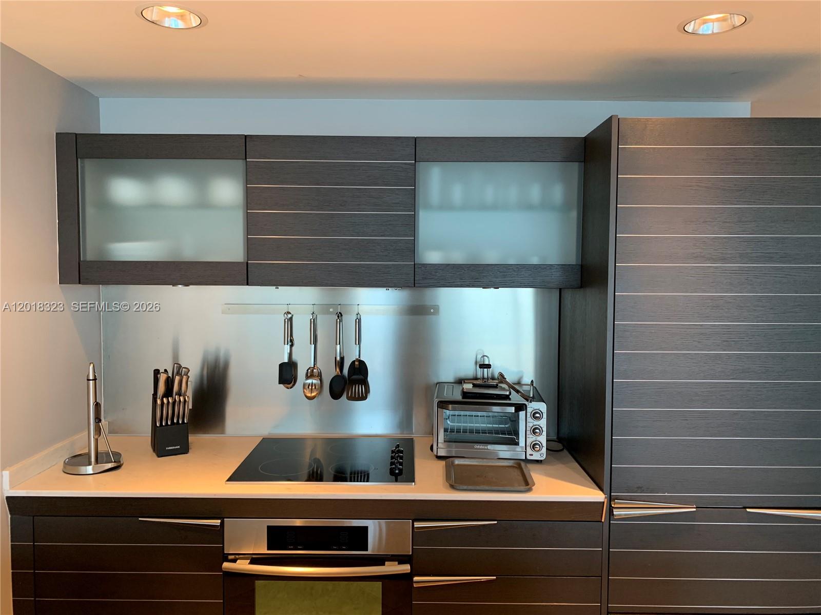 A modern kitchen features dark wood cabinetry, a stainless steel backsplash, and a glass cooktop — 200 Biscayne Boulevard Way # 4212, Miami FL 33131, MIAMI, FL