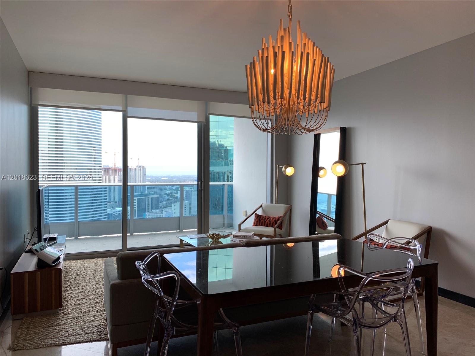 A dining and living area features a modern chandelier, glass table, and floor-to-ceiling windows — 200 Biscayne Boulevard Way # 4212, Miami FL 33131, MIAMI, FL