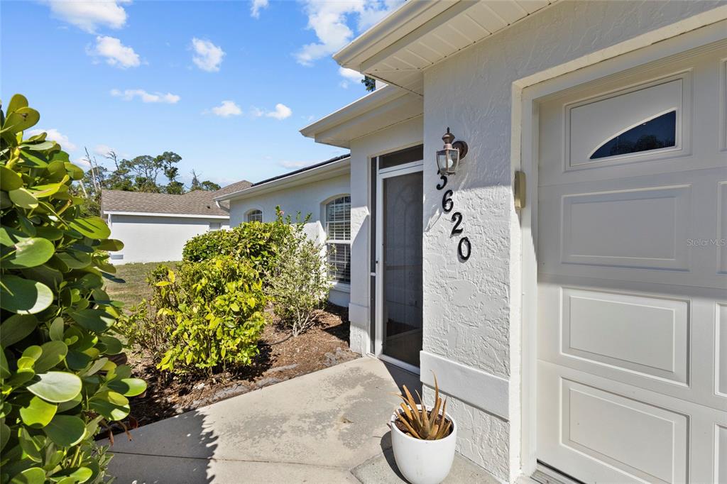 A white stucco house exterior features a front door, a garage, and house number 3620 — 3620 CANDIA AVENUE, NORTH PORT, FL