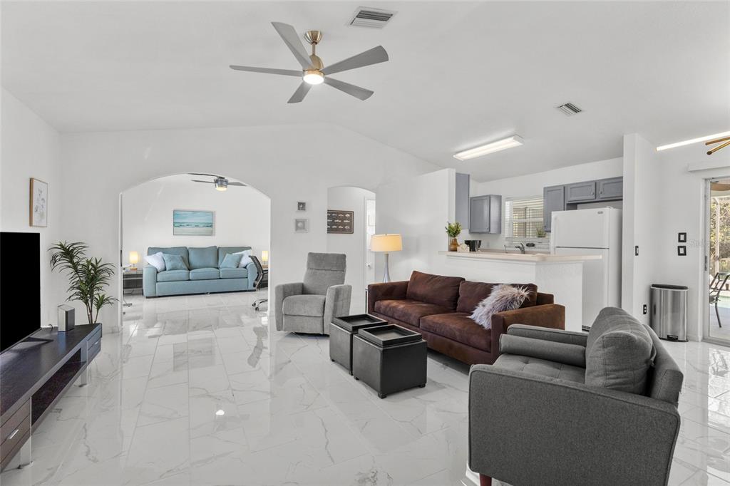 A living room with white tile floors, a brown sofa, and an open kitchen area — 3620 CANDIA AVENUE, NORTH PORT, FL