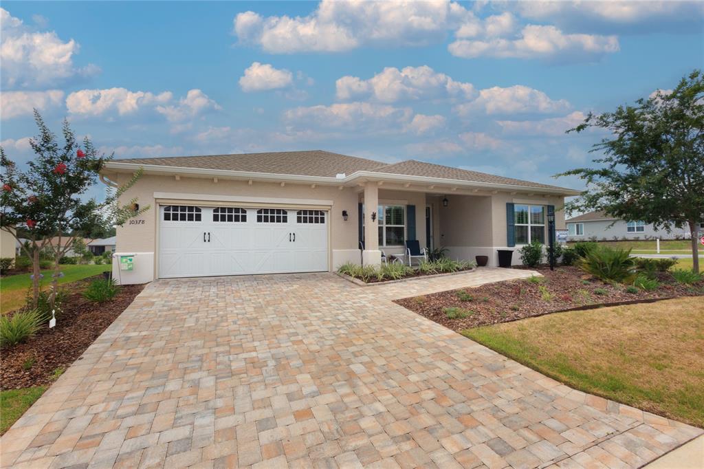 A single-story house with a beige stucco exterior, a paver driveway, and a two-car garage — 10378 SW 96TH LOOP, OCALA, FL