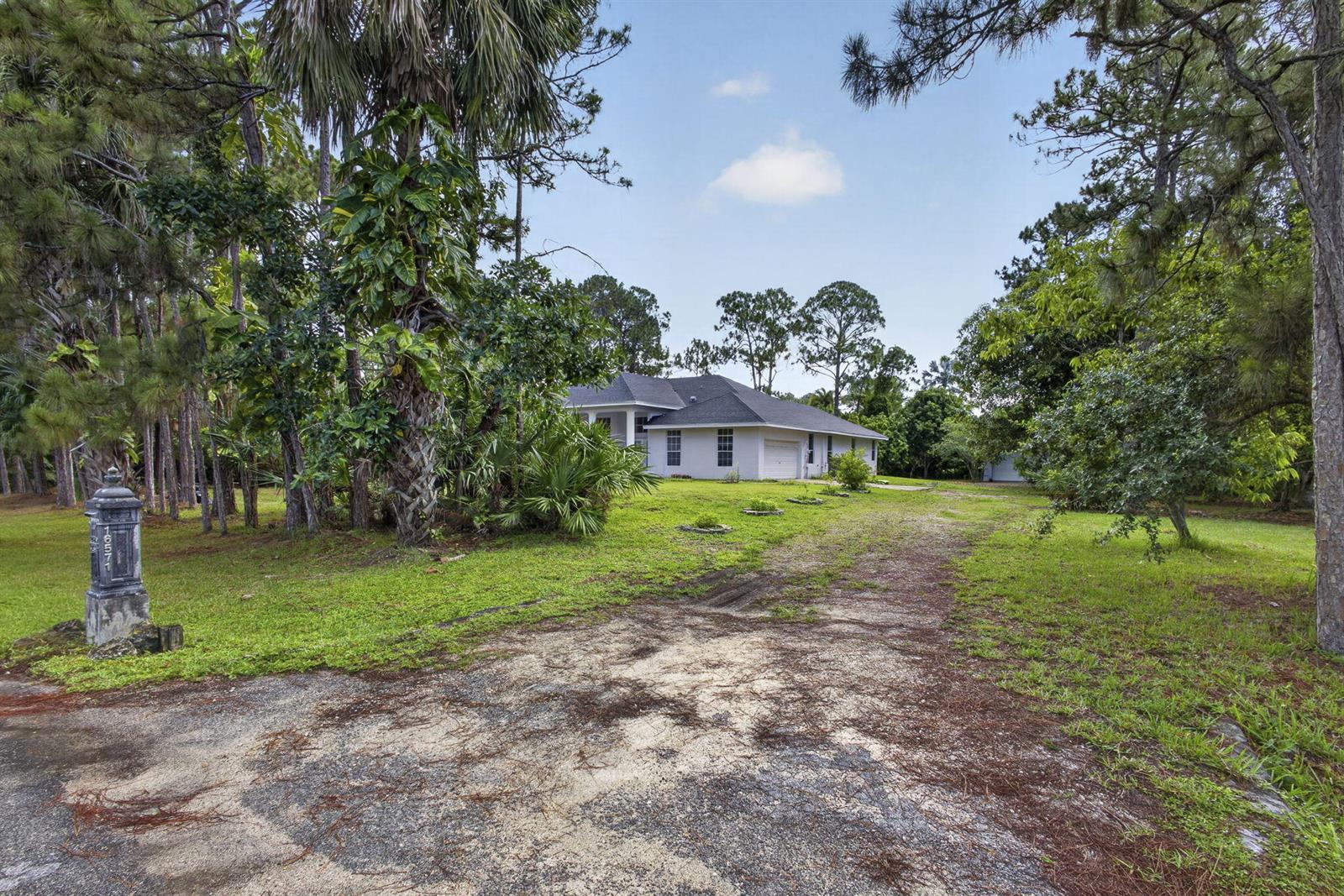 A single-story house with a white exterior sits at the end of a long driveway — 16571 78th Road N, FL 33470, FL