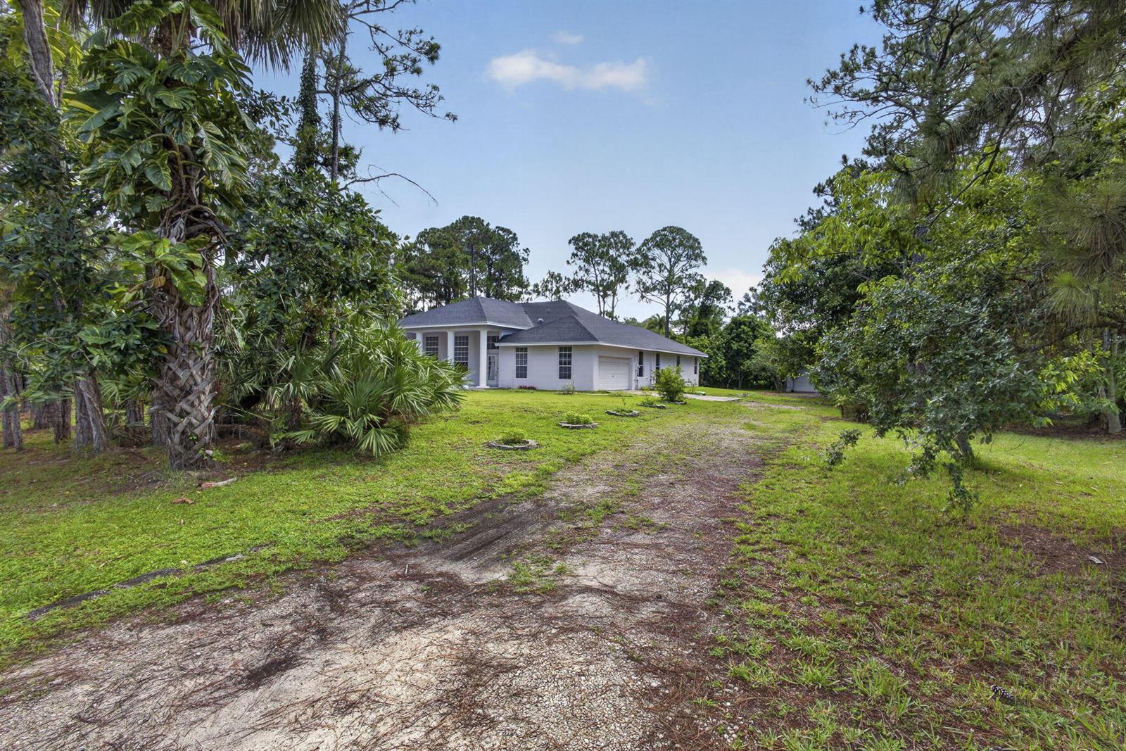 A single-story house with a white exterior and a gravel driveway sits among trees — 16571 78th Road N, FL 33470, FL
