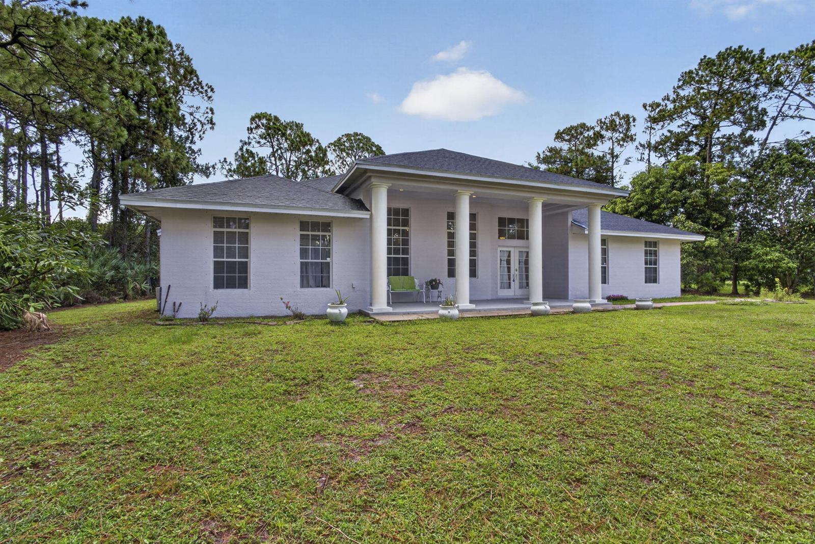 A white, single-story house with a columned front porch sits on a grassy lawn — 16571 78th Road N, FL 33470, FL