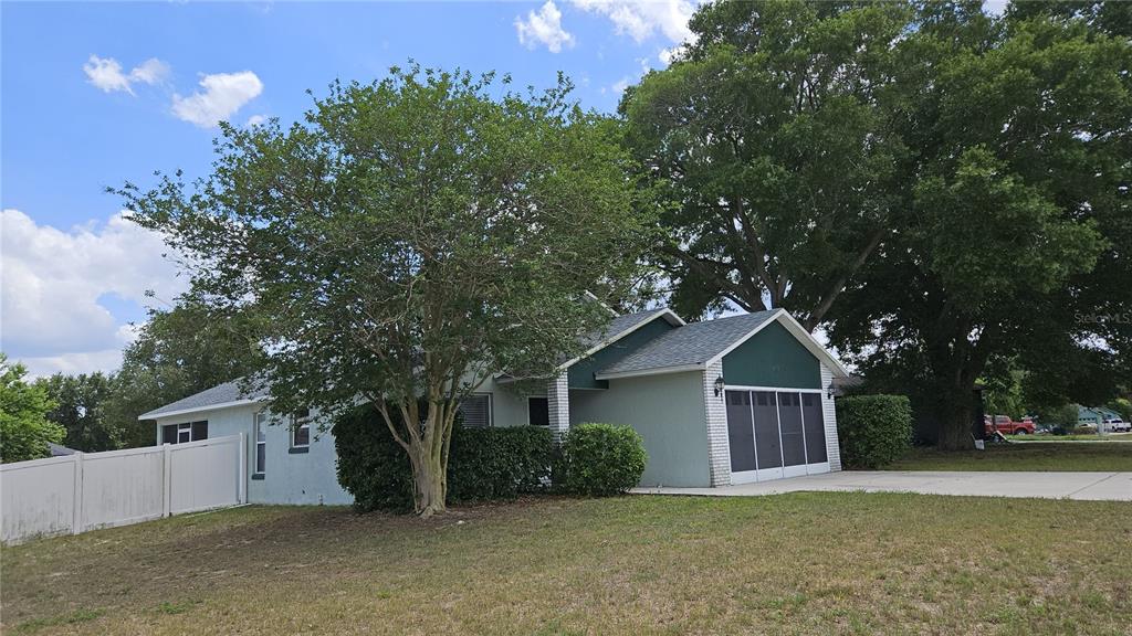 A single-story house with a light-colored exterior, a garage, and large trees in the yard — 108 BRITTANY AVENUE, MASCOTTE, FL