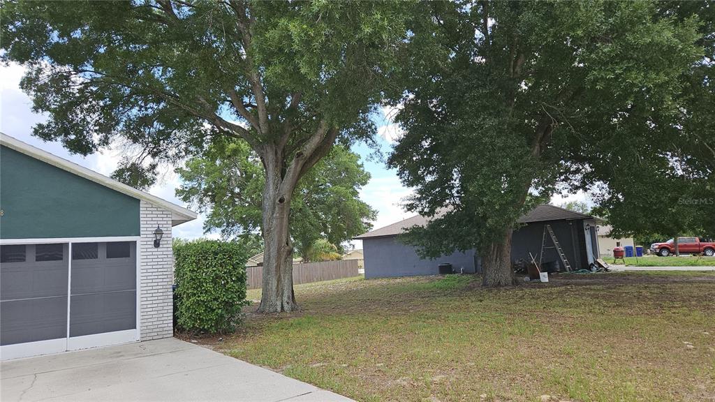 A view of a residential driveway, a garage, and large trees in a grassy yard — 108 BRITTANY AVENUE, MASCOTTE, FL