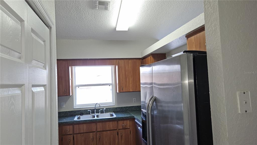 A kitchen features wood cabinets, a stainless steel refrigerator, and a double-basin sink — 108 BRITTANY AVENUE, MASCOTTE, FL
