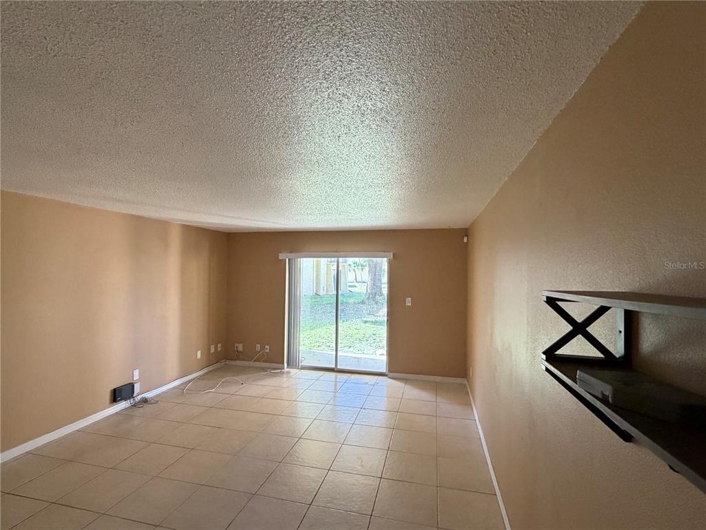 An empty living room features tan walls, tile flooring, and a sliding glass door — 7513 ABONADO RD UNIT 7513, TAMPA, FL
