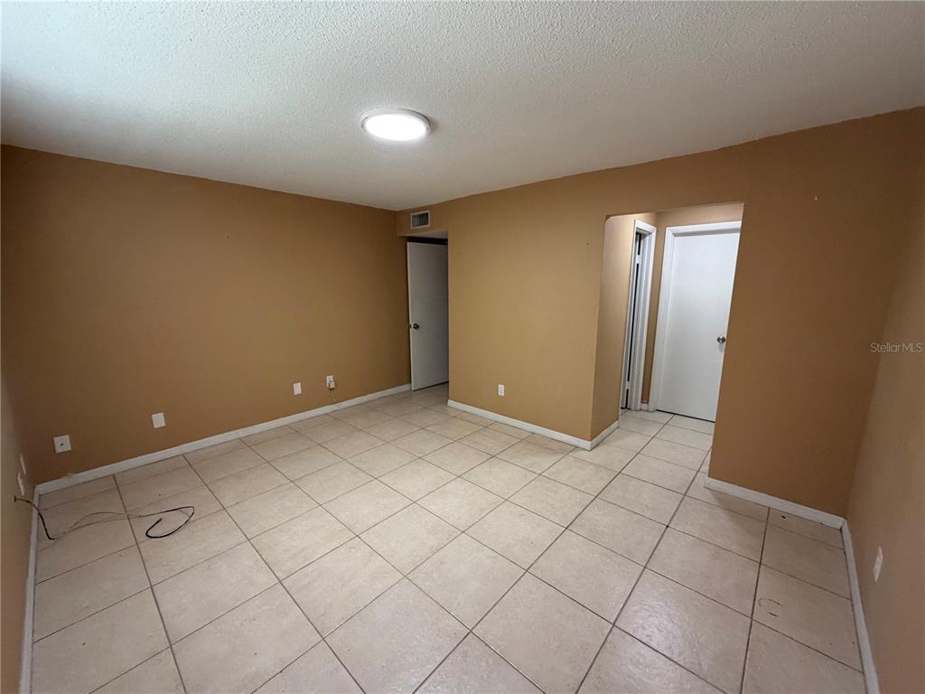 An empty room with tan walls, white trim, and light-colored square floor tiles — 7513 ABONADO RD UNIT 7513, TAMPA, FL
