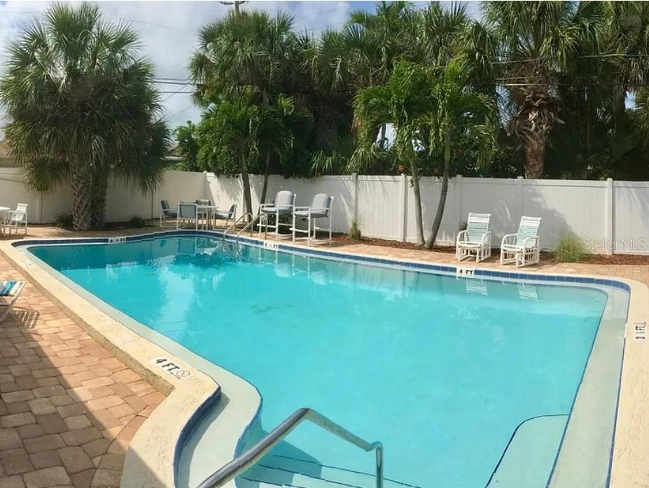 A rectangular swimming pool with a paved deck, lounge chairs, and palm trees in the background — 9030 BLIND PASS ROAD UNIT C7, ST PETERSBURG, FL