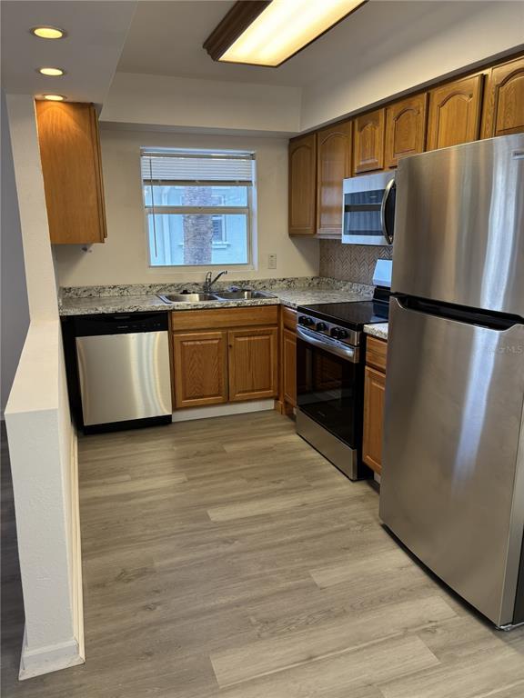 A kitchen features wood cabinets, granite countertops, stainless steel appliances, and light-colored wood-look flooring — 9030 BLIND PASS ROAD UNIT C7, ST PETERSBURG, FL
