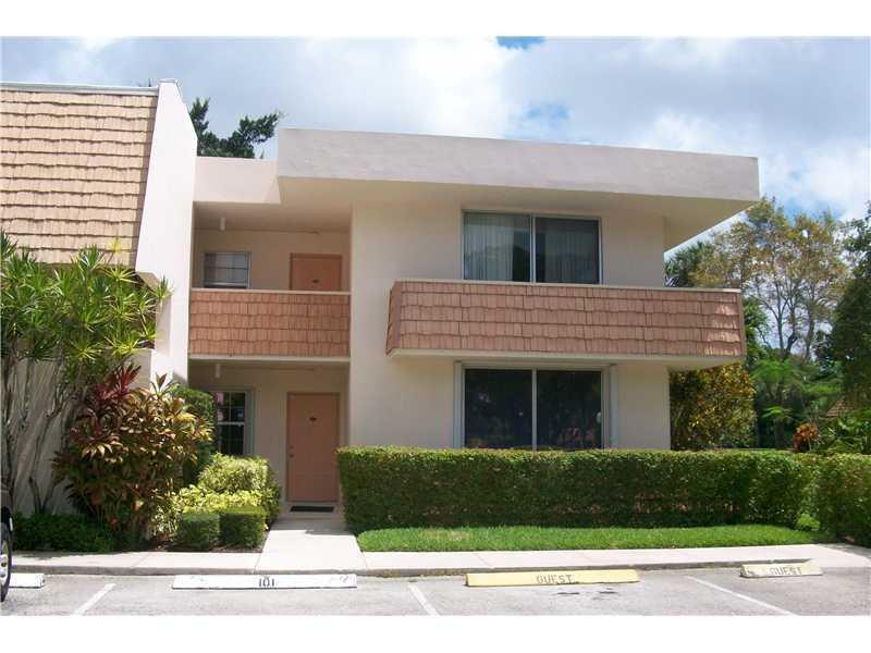 A two-story apartment building features tan stucco walls, brown shingle accents, and a hedge-lined parking area — 4031 N Cypress Drive # 101, Pompano Beach FL 33069, POMPANO BEACH, FL