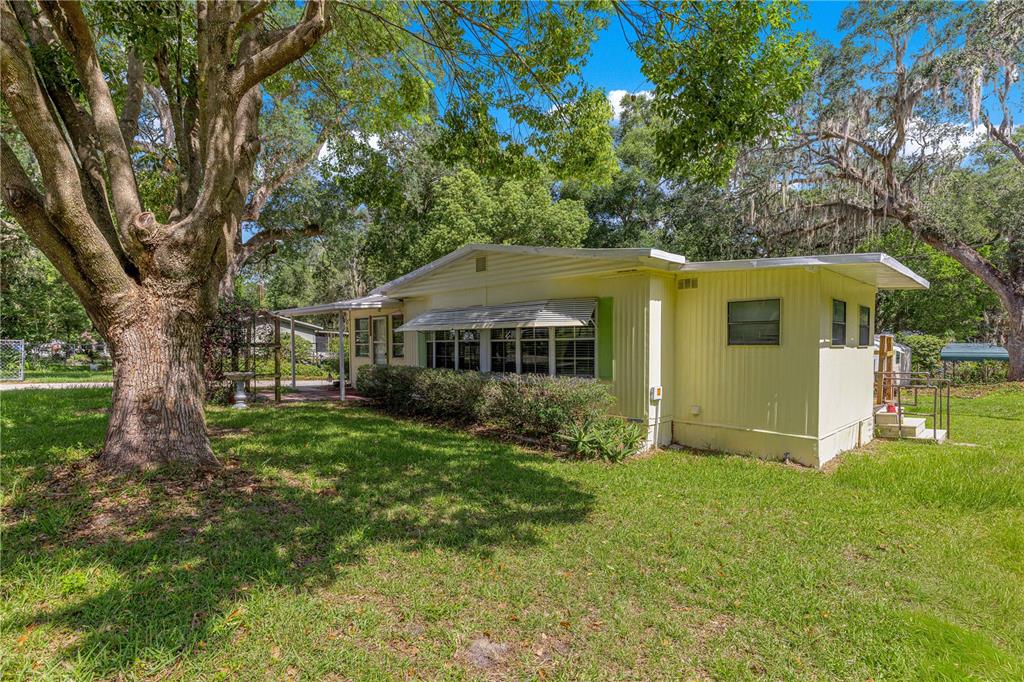 A light yellow mobile home sits on a grassy lot shaded by large oak trees — 10495 SE 130TH LANE, OCKLAWAHA, FL