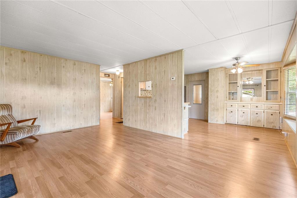 A living room with wood-paneled walls, light wood flooring, and a built-in hutch — 10495 SE 130TH LANE, OCKLAWAHA, FL