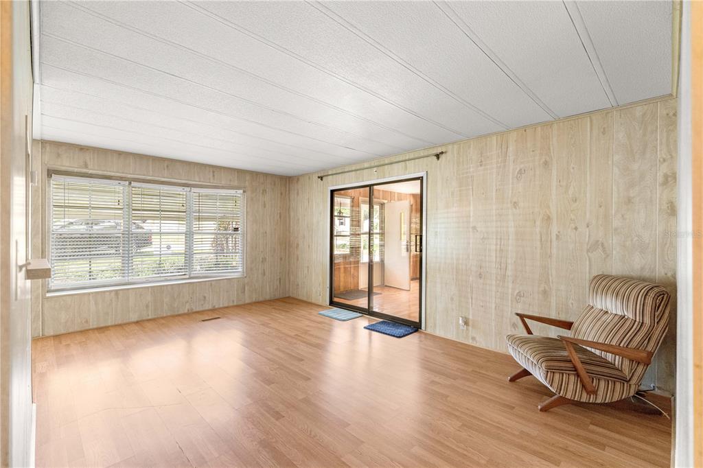 A room with wood-paneled walls, light wood flooring, a large window, and a sliding door — 10495 SE 130TH LANE, OCKLAWAHA, FL