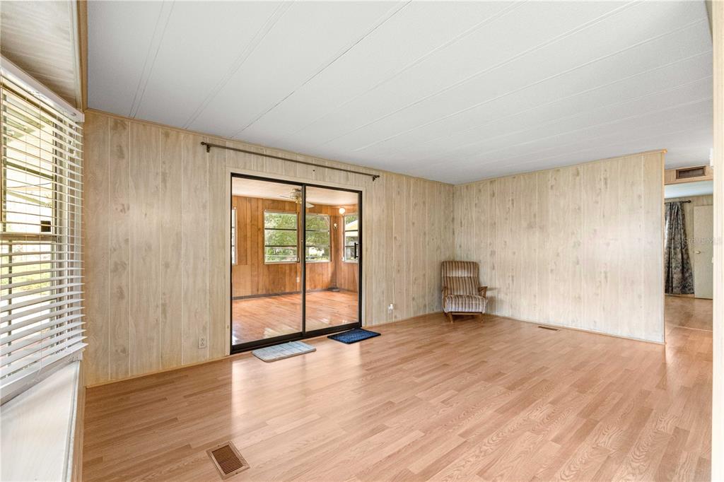 A living room with wood-paneled walls, light wood flooring, and a sliding glass door — 10495 SE 130TH LANE, OCKLAWAHA, FL