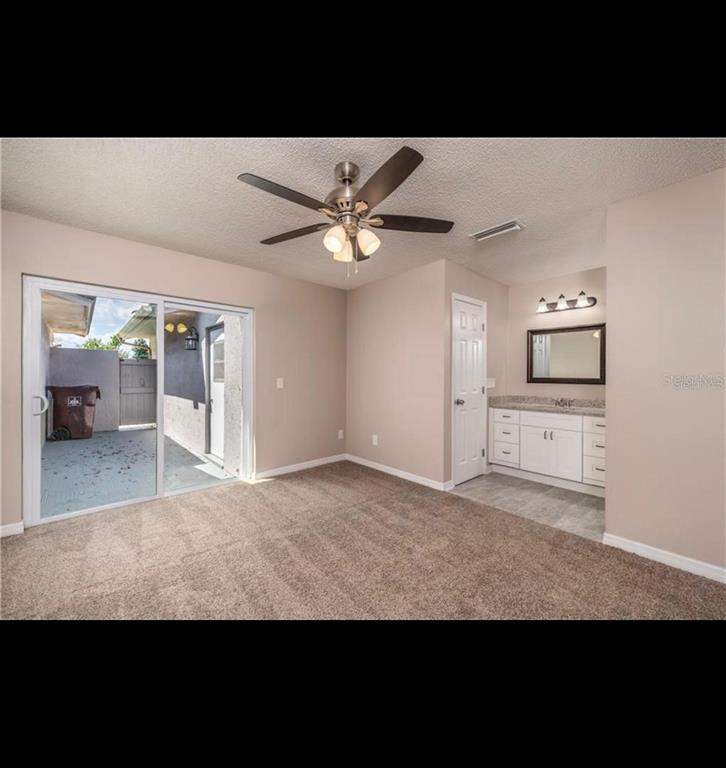 A bedroom with carpeted flooring, a ceiling fan, sliding glass doors, and an attached vanity — 5409 SERENE LANE, ORLANDO, FL