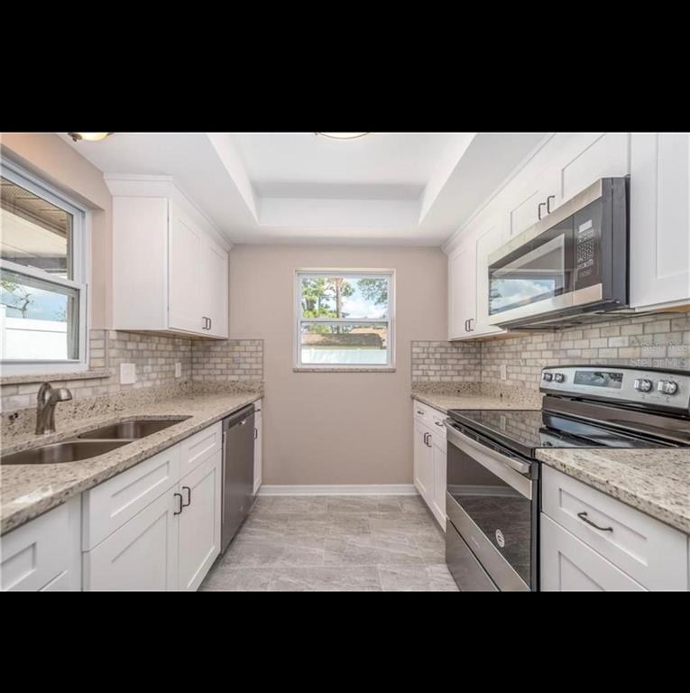 A galley kitchen features white cabinets, granite countertops, stainless steel appliances, and a tiled backsplash — 5409 SERENE LANE, ORLANDO, FL