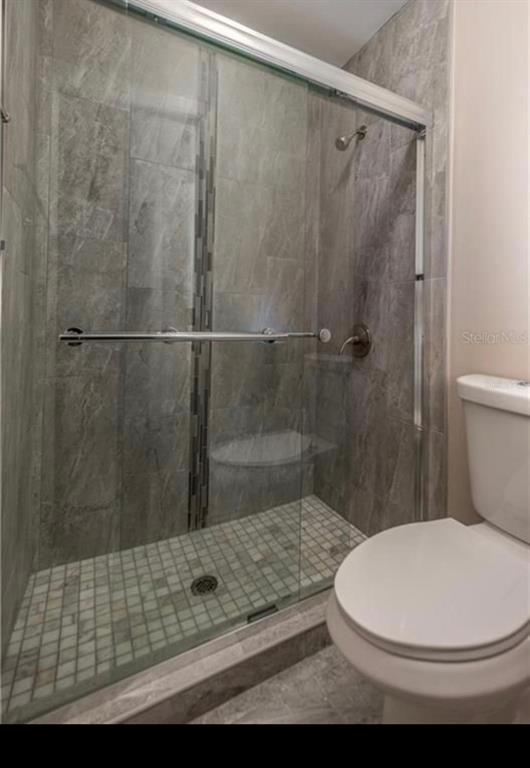 A bathroom features a glass-enclosed walk-in shower with gray stone tile and a white toilet — 5409 SERENE LANE, ORLANDO, FL