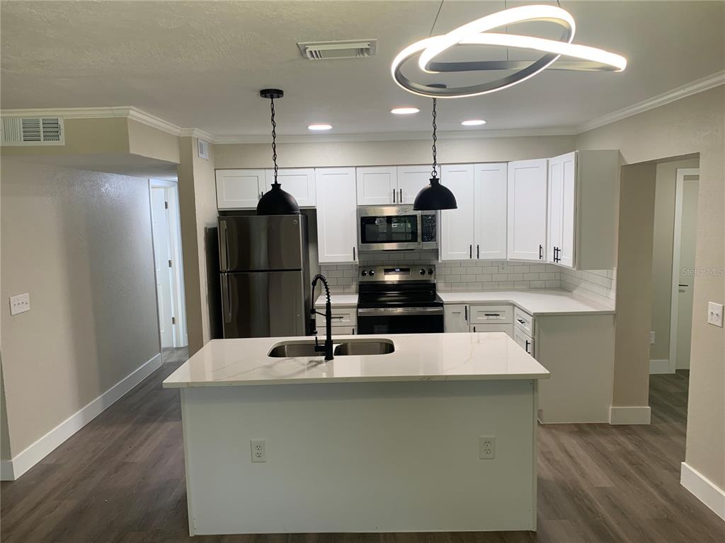 A modern kitchen features white cabinets, stainless steel appliances, a center island, and wood flooring — 1915 WEEKS AVENUE, ORLANDO, FL