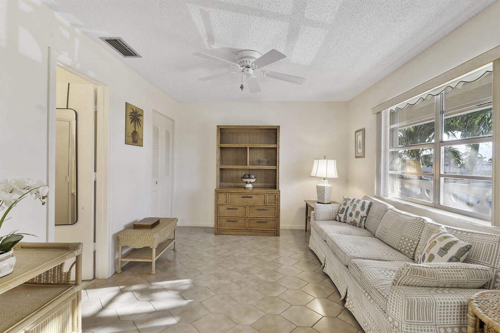 A living room features tile flooring, a patterned sofa, a wooden hutch, and a ceiling fan — 1050 Citrus # 202, Delray Beach FL 33445, DELRAY BEACH, FL