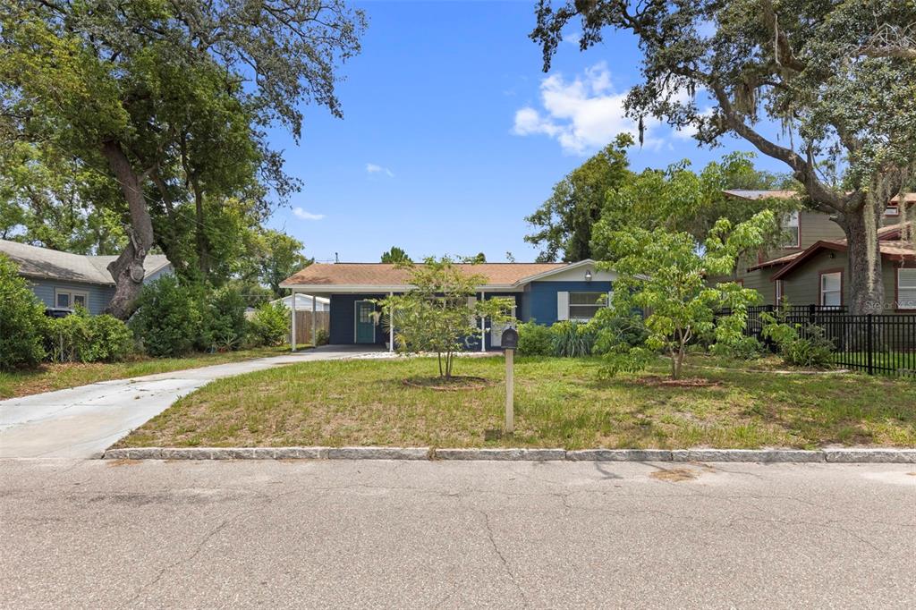 A single-story blue house with a carport sits behind a lawn with two small trees — 1218 E NEW ORLEANS AVENUE, TAMPA, FL