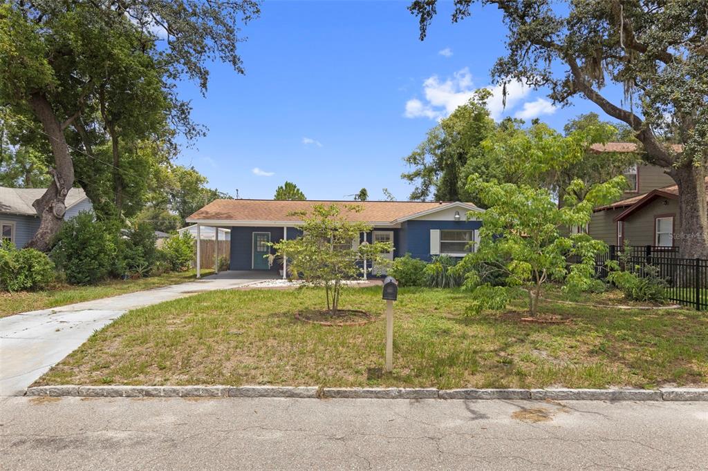 A blue single-story house with a carport and a front yard sits under large trees — 1218 E NEW ORLEANS AVENUE, TAMPA, FL