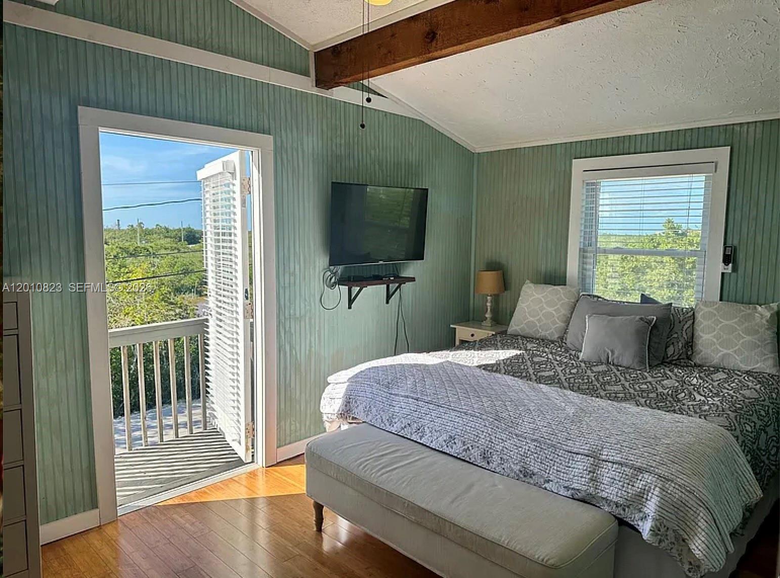 A bedroom features light green vertical paneling, a wooden ceiling beam, and a balcony door — 813 Hawksbill Ln, Sugarloaf FL 33042, SUGARLOAF, FL