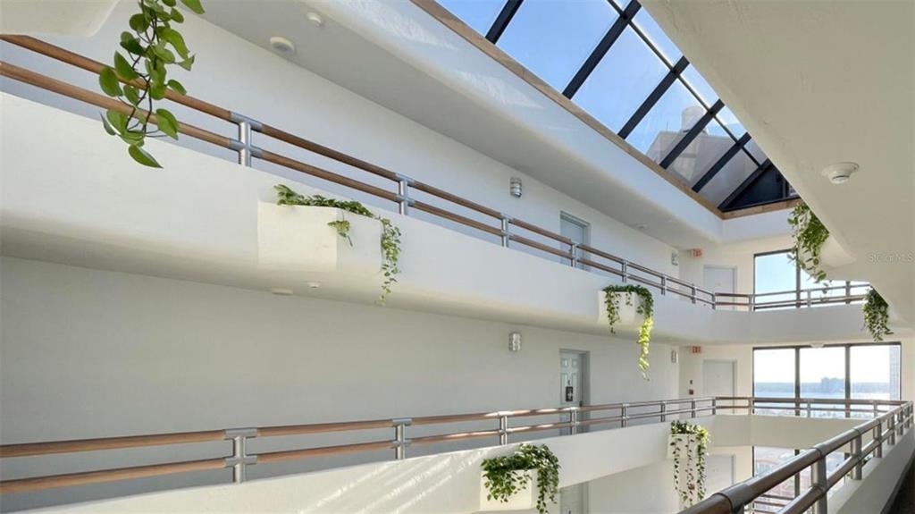 An indoor atrium with multiple levels, white walls, wooden railings, and hanging plants under skylights — 3023 S ATLANTIC AVENUE UNIT 903, DAYTONA BEACH, FL