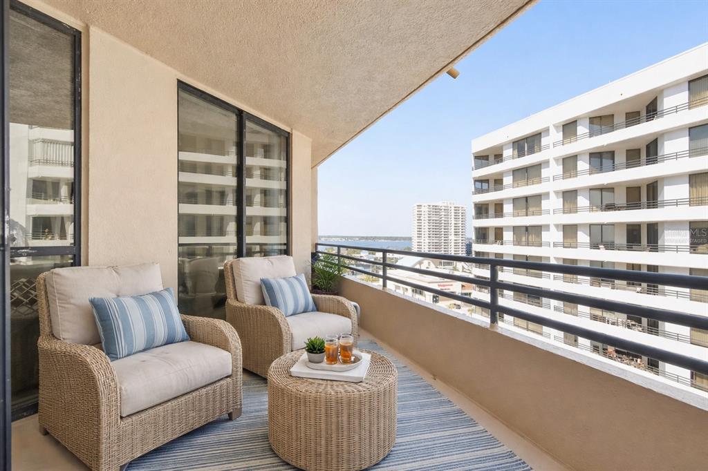 A balcony with two wicker chairs, a matching round table, and a view of buildings — 3023 S ATLANTIC AVENUE UNIT 903, DAYTONA BEACH, FL