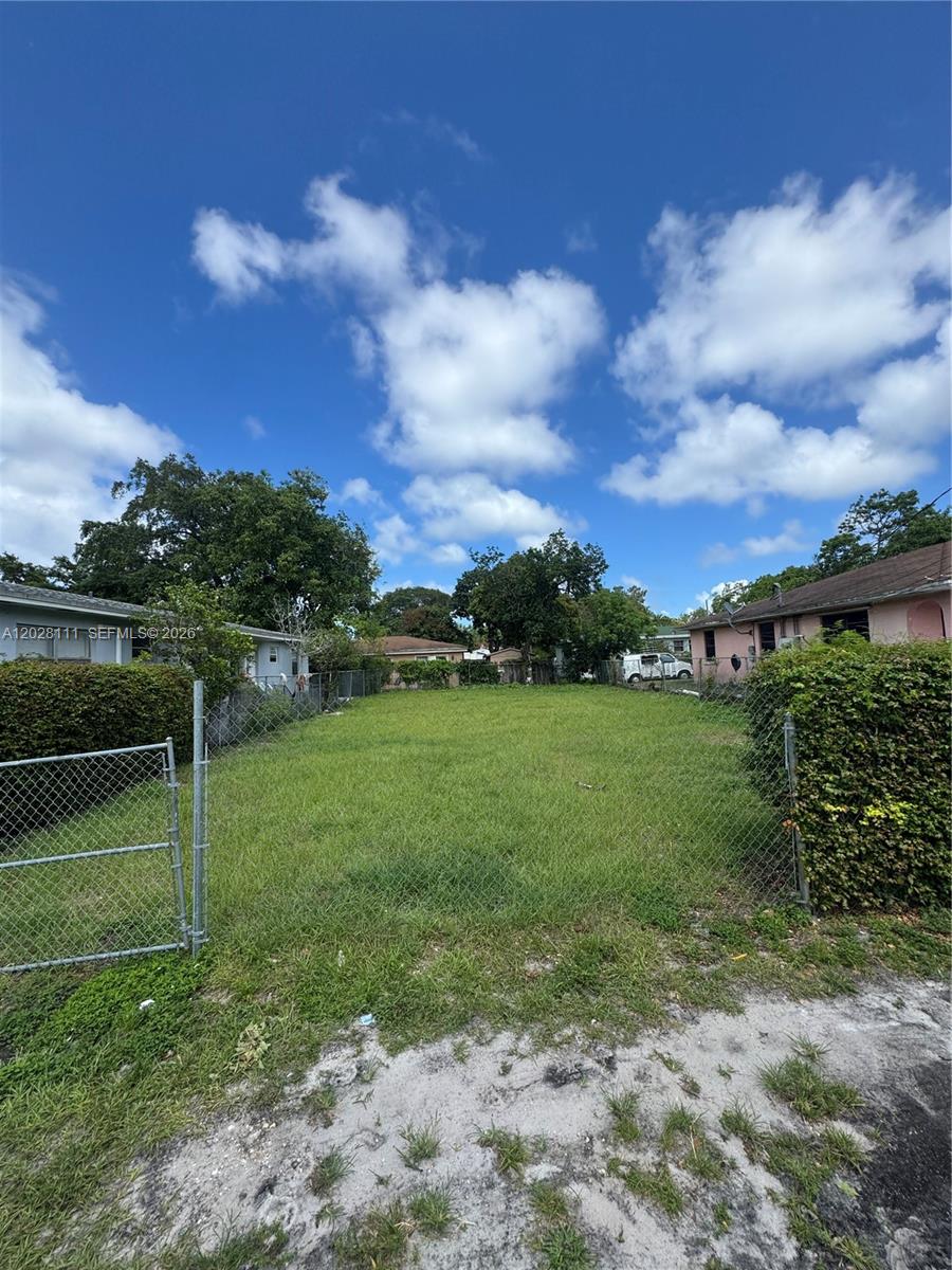 A fenced, grassy vacant lot is situated between two residential houses under a blue sky — 6335 NW 1st Ct, Miami FL 33150, MIAMI, FL