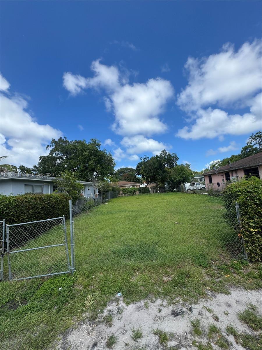 A fenced, grassy vacant lot is situated between two residential houses under a blue sky — 6335 NW 1st Ct, Miami FL 33150, MIAMI, FL