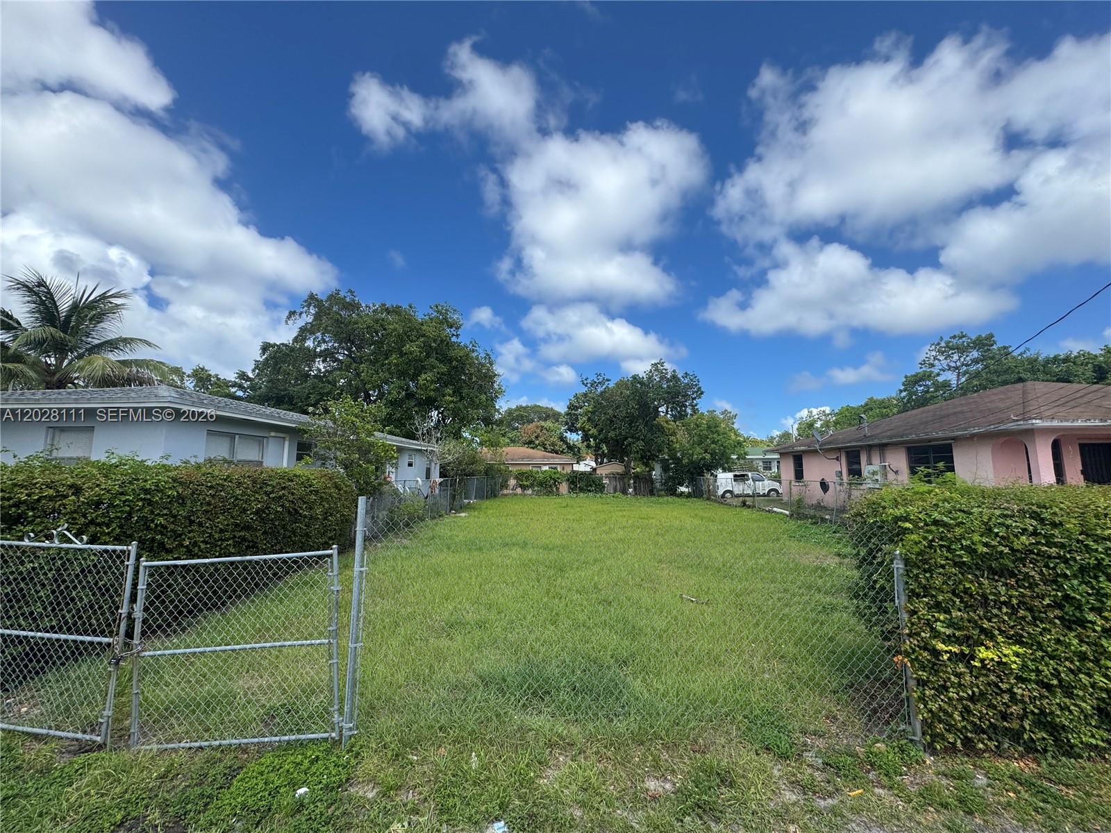 A vacant, grass-covered residential lot is enclosed by chain-link fencing between two houses — 6335 NW 1st Ct, Miami FL 33150, MIAMI, FL