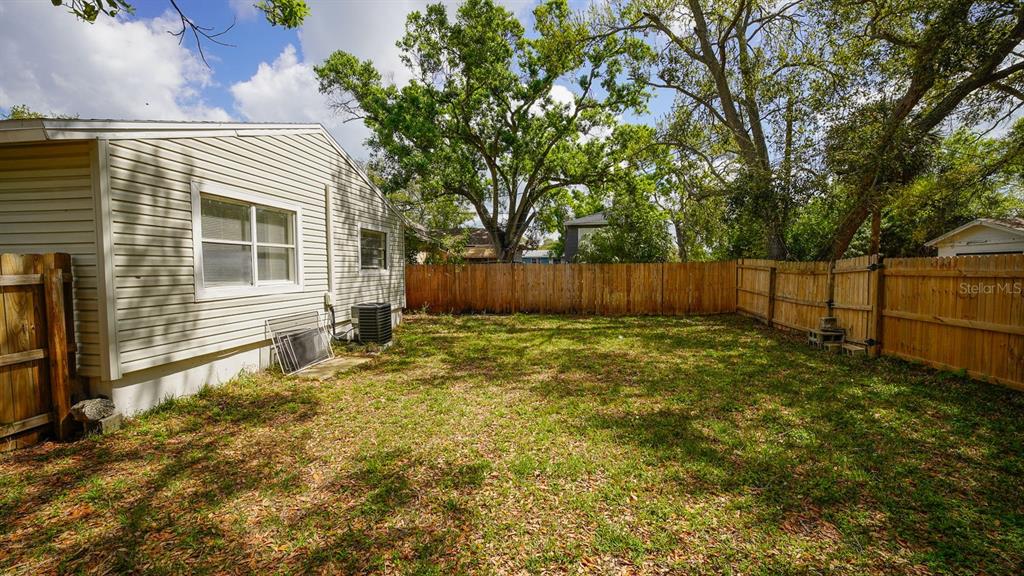 A backyard with a light-colored siding house, a wooden fence, and several large trees — 546 16TH AVENUE S, ST PETERSBURG, FL