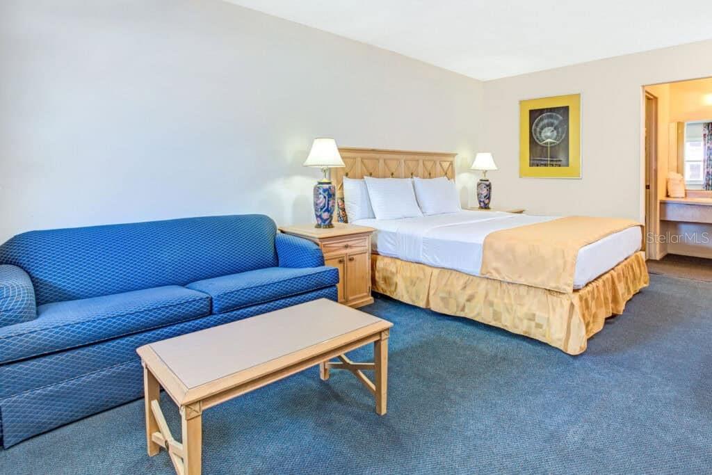 A hotel room features a blue sofa, a coffee table, and a bed with yellow bedding — 4651 W IRLO BRONSON MEMORIAL HIGHWAY, KISSIMMEE, FL