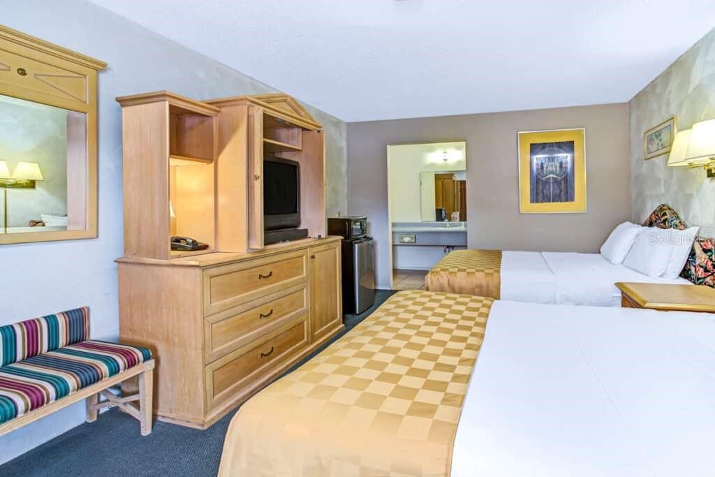 A hotel room features two beds, a wooden dresser with a television, and a small bench — 4651 W IRLO BRONSON MEMORIAL HIGHWAY, KISSIMMEE, FL