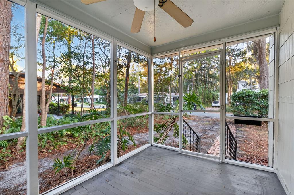 A screened-in porch with a gray wooden floor, ceiling fan, and views of wooded surroundings — 914 NE 6TH AVENUE, GAINESVILLE, FL