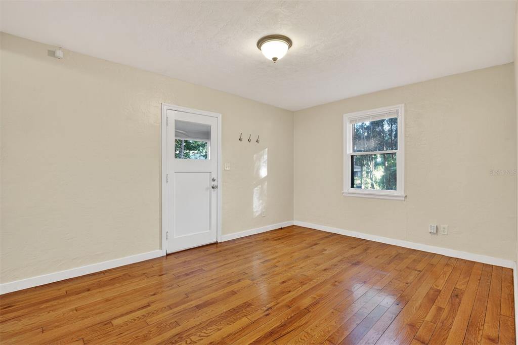 An empty room features hardwood floors, beige walls, a white door, and a single window — 914 NE 6TH AVENUE, GAINESVILLE, FL