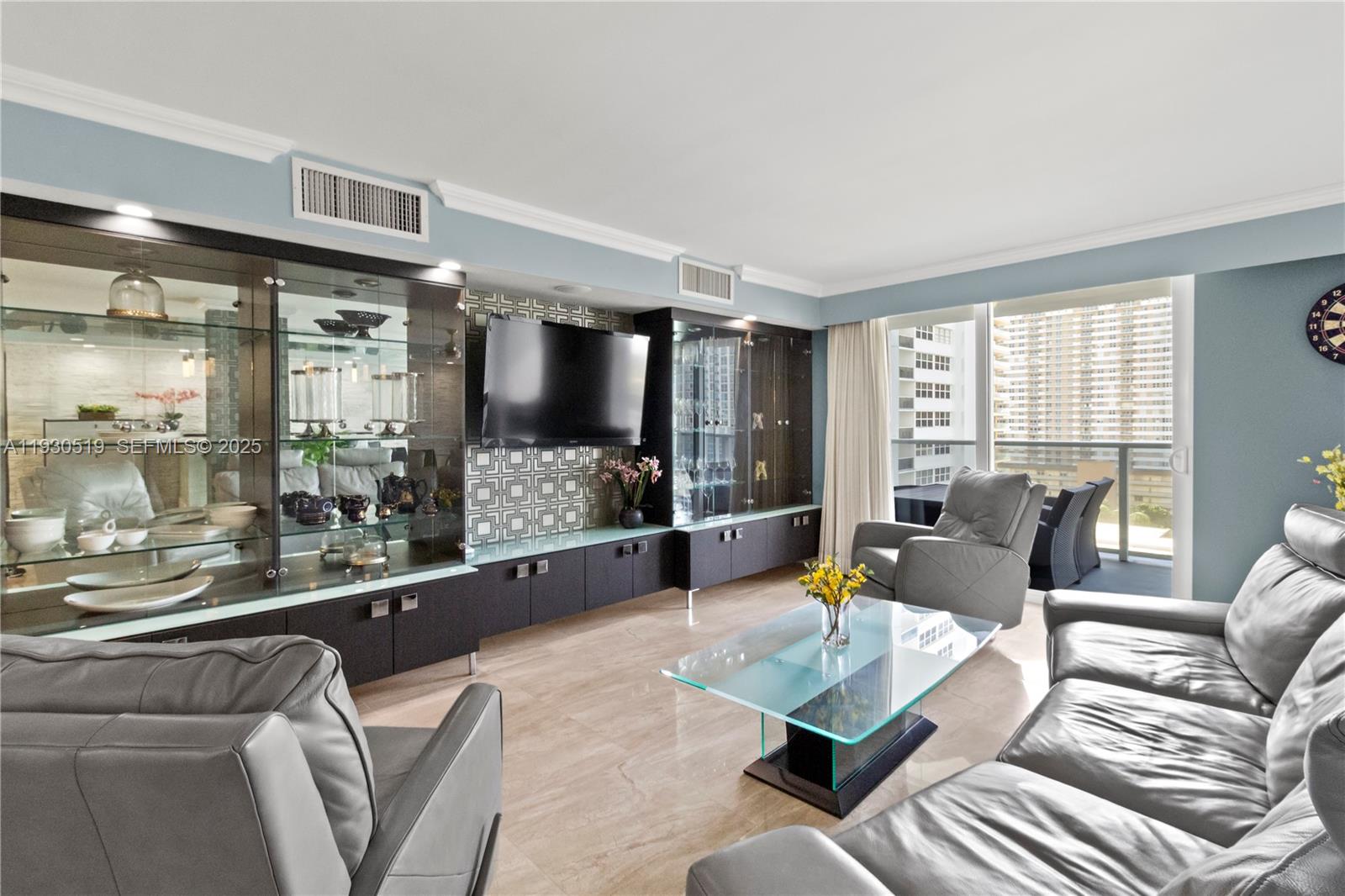 A living room features gray leather furniture, a glass coffee table, and built-in display cabinetry — 1880 S Ocean Dr, Hallandale Beach FL 33009, HALLANDALE BEACH, FL
