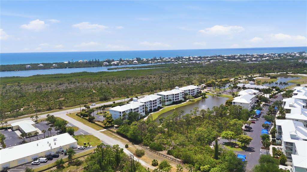 An aerial view shows multi-story apartment buildings surrounded by greenery, a pond, and nearby water — 8405 PLACIDA ROAD UNIT 204, PLACIDA, FL