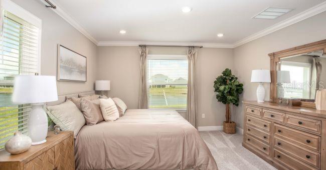 A bedroom features a bed with neutral bedding, a wooden dresser, and windows overlooking water — 3880 BLUETHREAD WAY, POINCIANA, FL