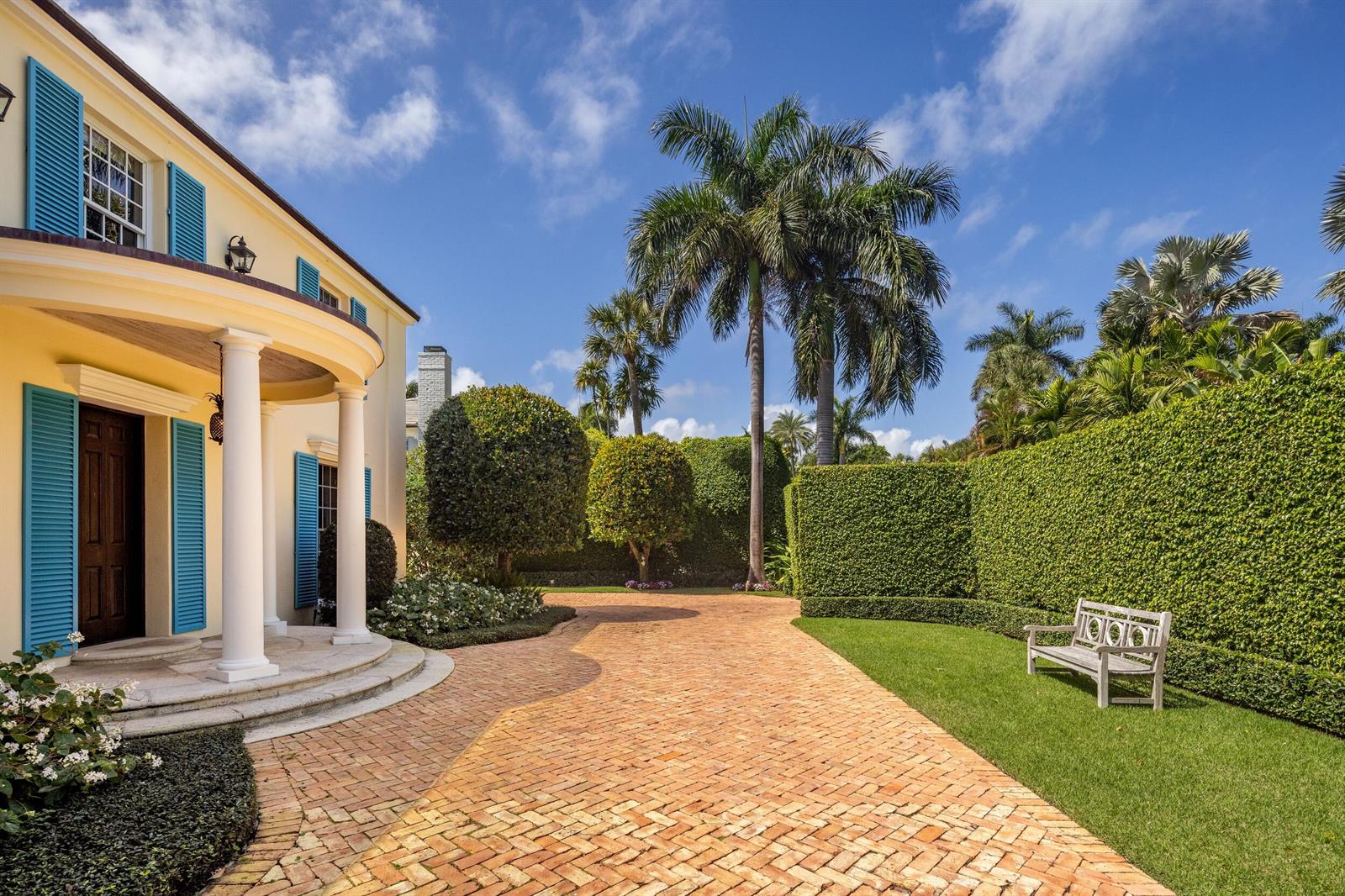 A brick driveway leads to the entrance of a yellow house with blue shutters — 246 Emerald Lane, Palm Beach FL 33480, PALM BEACH, FL